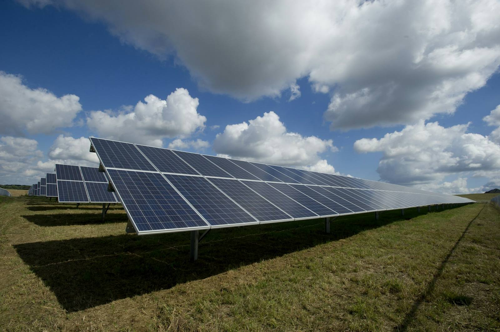 Filas de módulos solares en una planta en suelo bajo nubes